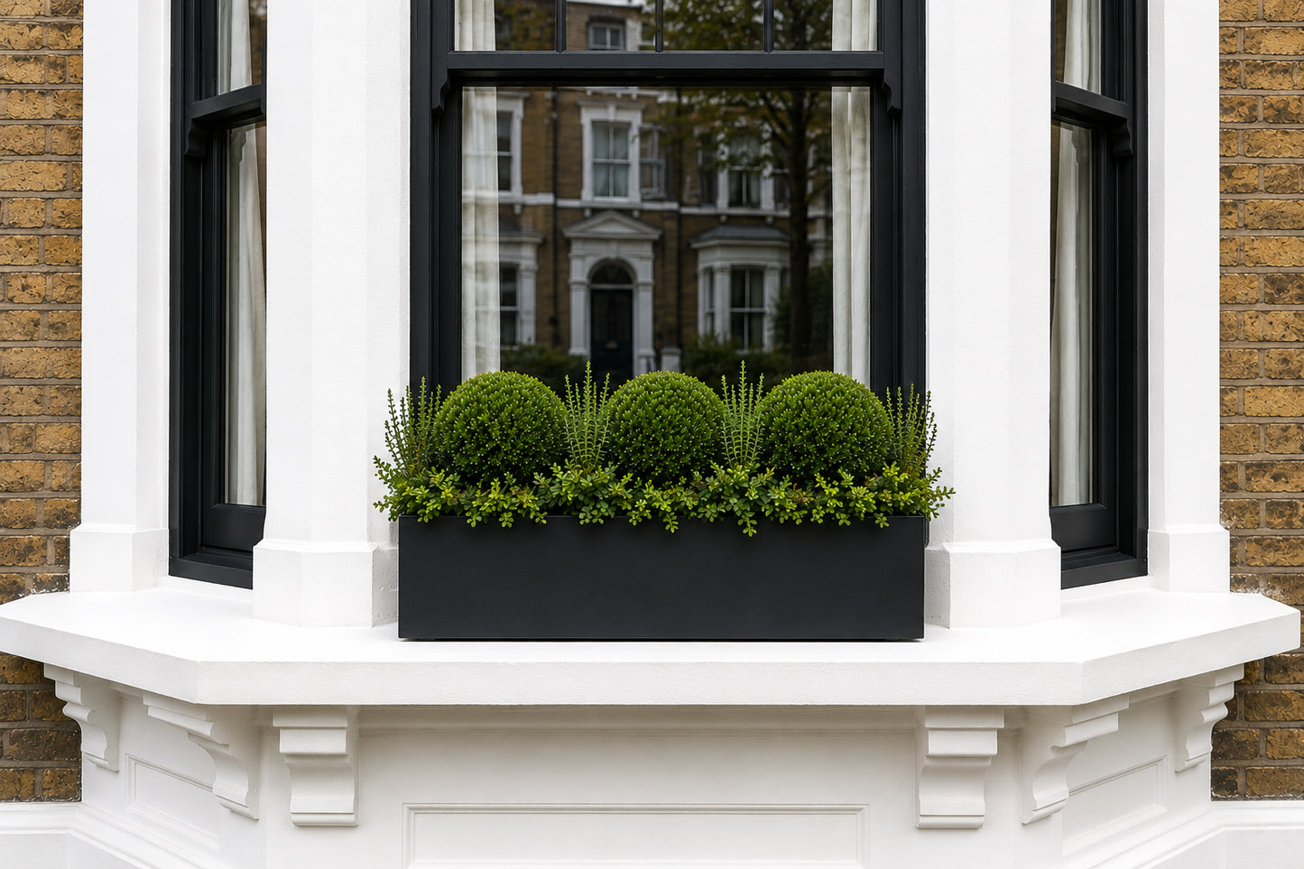 Window box with green plants on a decorative window ledge of a brick building.