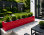 Modern outdoor garden with a red planter, grass, and a building in the background.